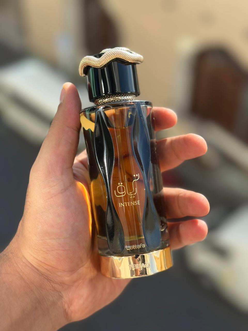 Hand holding a perfume bottle labeled 'Intense' with a blurred background